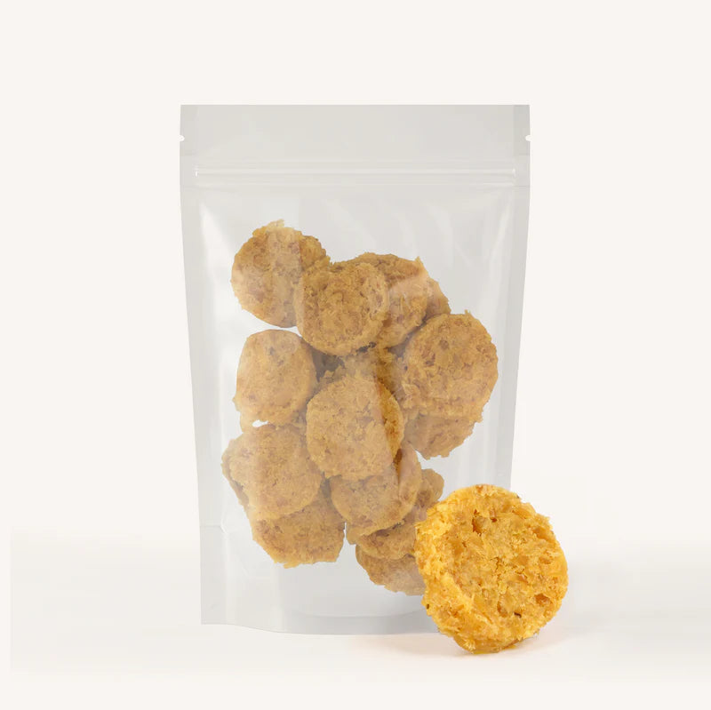 Clear resealable bag filled with round golden-brown dog treats made from green tripe chips on a white background