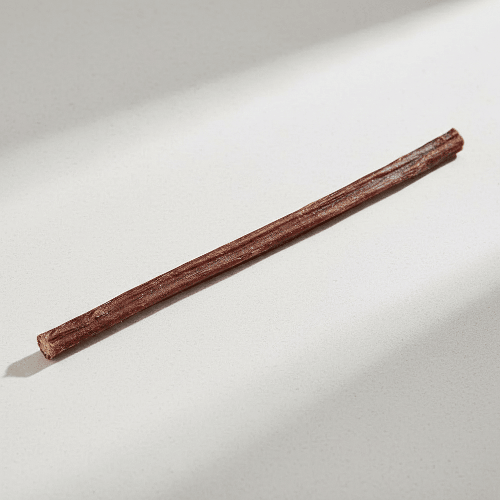 A single Home Range All-Natural Bully Stick, brown and long, lying diagonally on a light gray surface with shadows.
