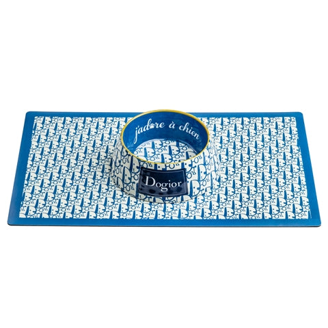 A blue and white monogrammed Dogior dog bowl sits on a matching rectangular placemat.