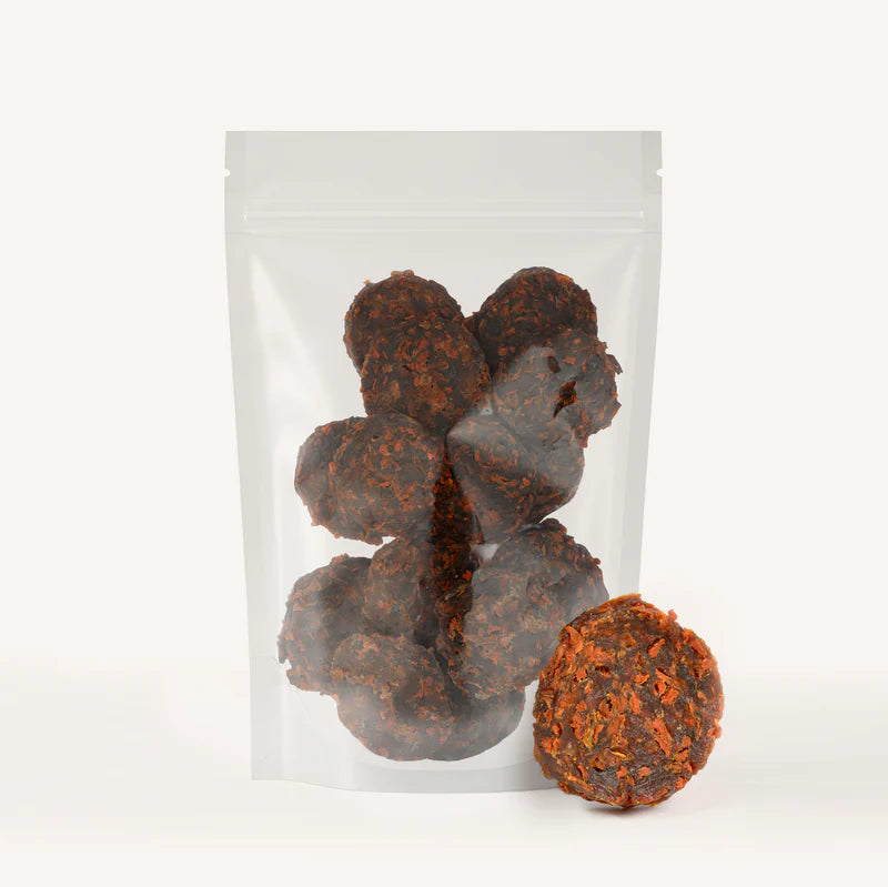 Clear bag containing round dark brown chicken and carrot dog treat chips with one chip placed outside the bag