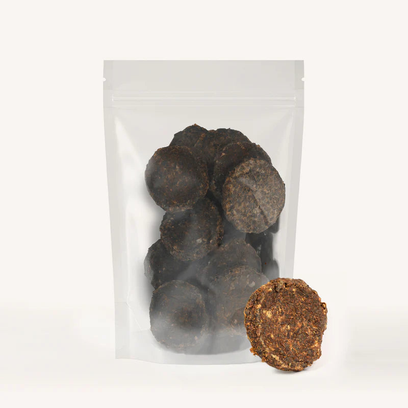 Clear resealable bag filled with round natural dark brown dog treats, one treat displayed outside the bag