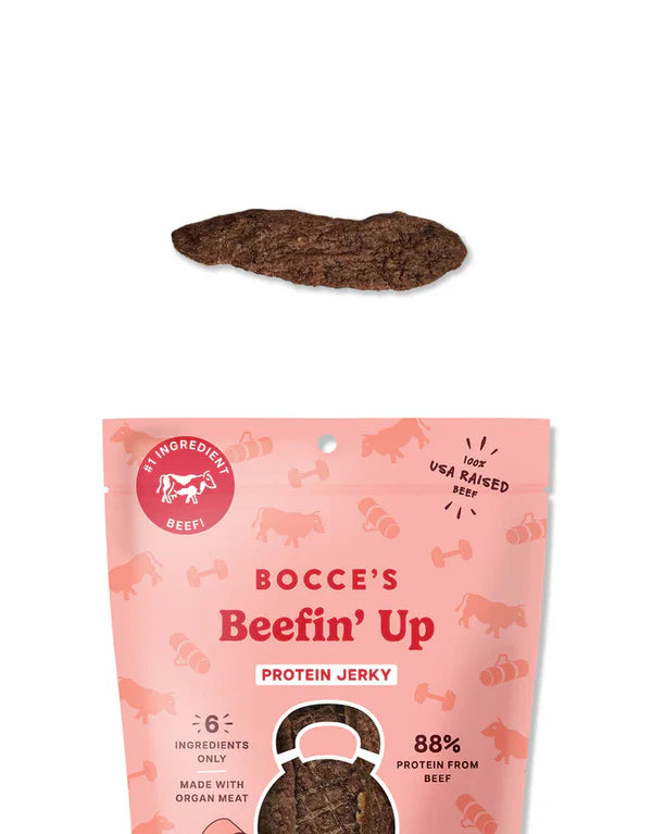 Bocce's Bakery Beefin' Up Jerky Protein Cuts 5oz, featuring a beef jerky piece above a pink packaging with a dog treat design