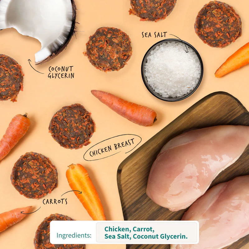 Round dog treat chips surrounded by fresh carrots, raw chicken breast, sea salt, and coconut pieces on beige background