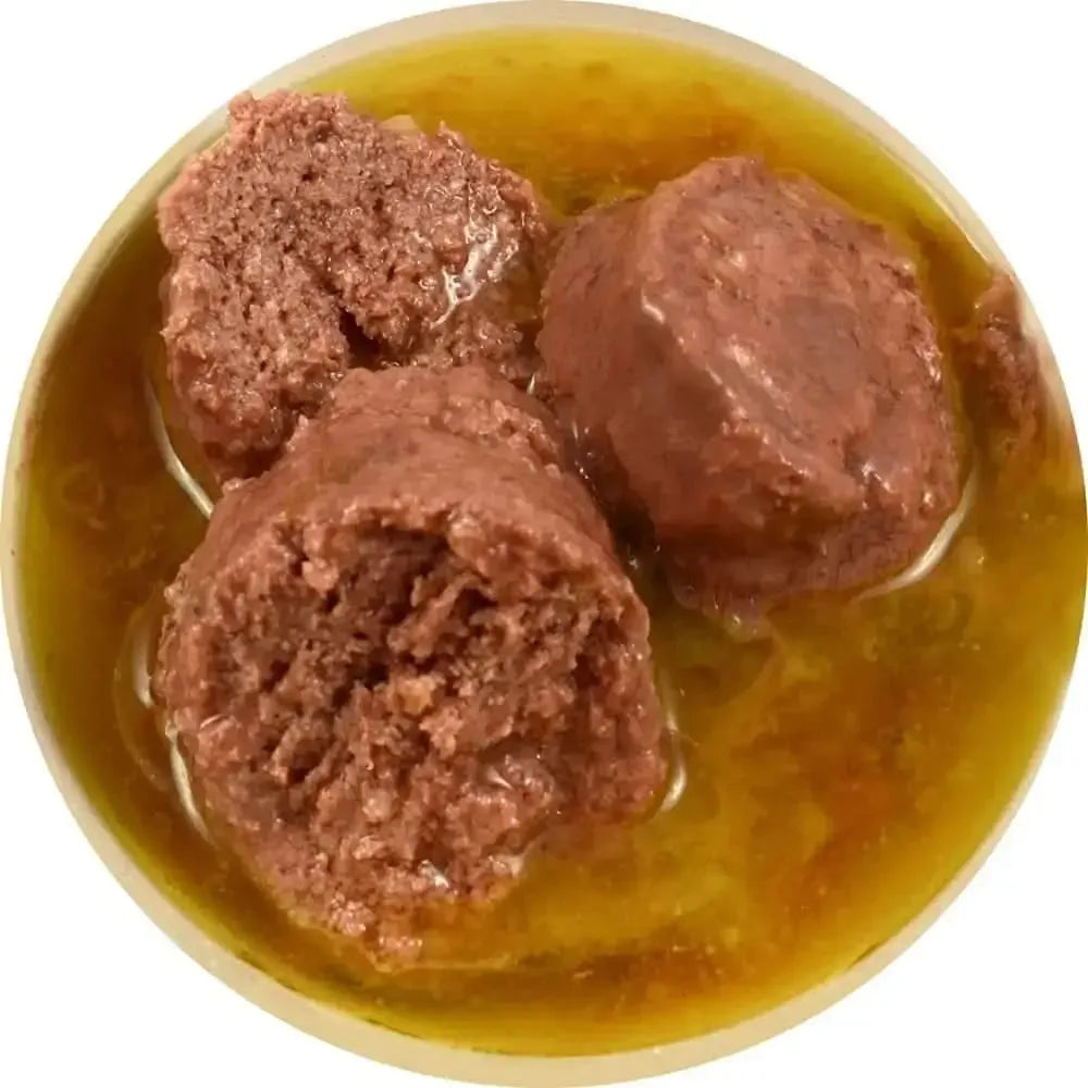 Three chunks of Against the Grain Nothing Else One Ingredient Duck Dog Food sit in yellowish gravy, viewed from above in a circular container.