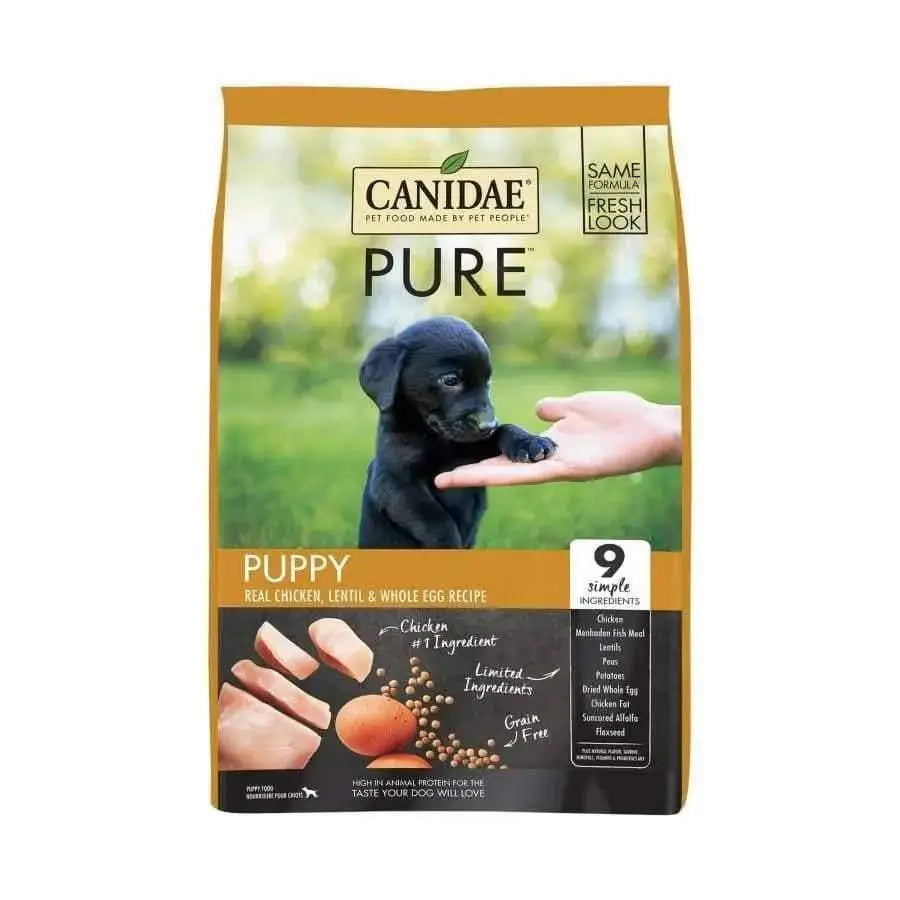 A bag of CANIDAE PURE Grain-Free Puppy Real Chicken, Lentil & Whole Egg Recipe Dry Dog Food shows a black puppy touching a person’s hand. This limited-ingredient recipe is grain-free and features chicken as the first of only 9 simple ingredients.
