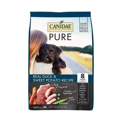A bag of CANIDAE PURE Grain-Free Real Duck & Sweet Potato Recipe dog food, featuring a woman with a black puppy. The label highlights “Real Duck & Sweet Potato,” 8 simple ingredients, and images of duck meat and sweet potatoes.
