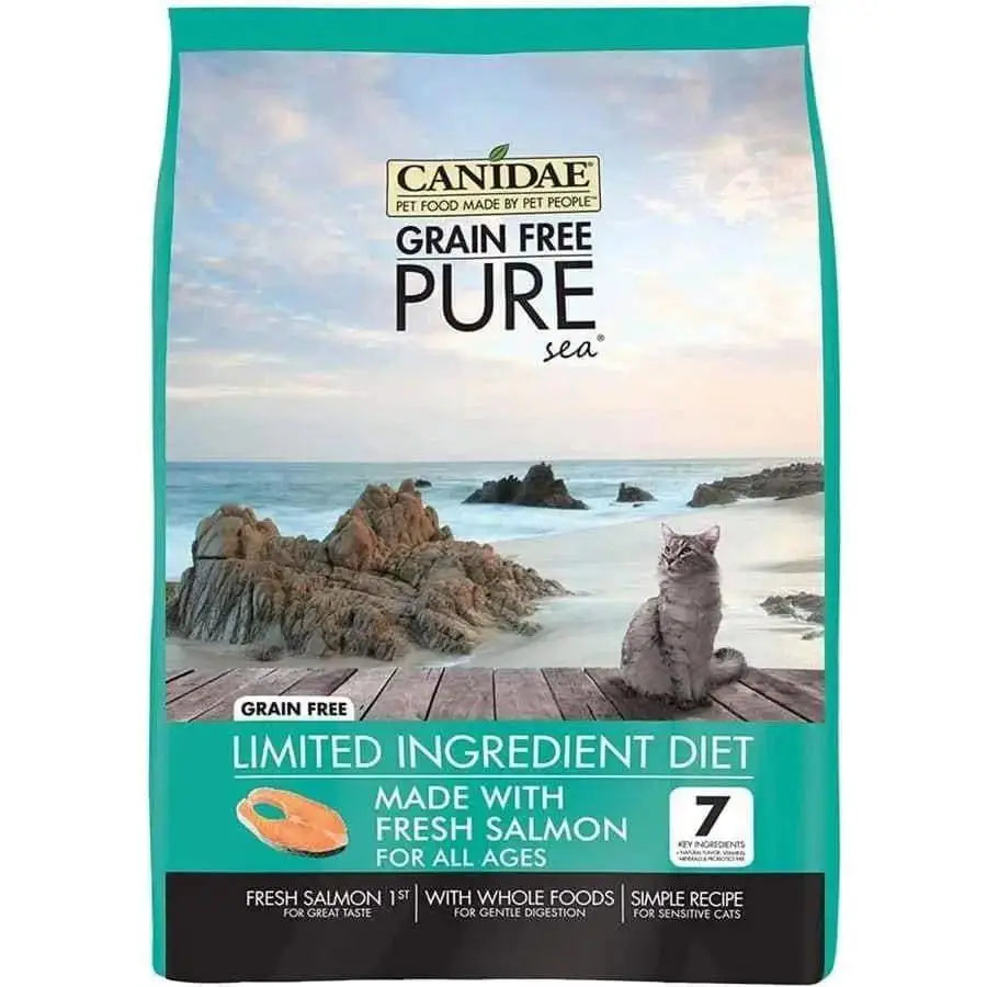 A teal and beige bag of CANIDAE PURE Sea Formula with Salmon Limited Ingredient Dry Cat Food rests on a rocky beach, emphasizing fresh salmon. Ideal for cats of all ages, it offers grain-free nutrition for sensitive felines.