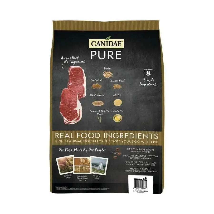 A mostly black and brown bag of CANIDAE PURE with Wholesome Grains Real Beef & Barley dry dog food, featuring raw beef images and ingredient icons. The label highlights 8 simple, real food ingredients for dogs.