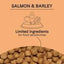 A label with CANIDAE PURE with Wholesome Grains Real Salmon & Barley Recipe Dry Dog Food features fish, heart, and leaf icons. Beneath, text notes limited ingredients for sensitivities. Brown kibble appears at the images bottom.