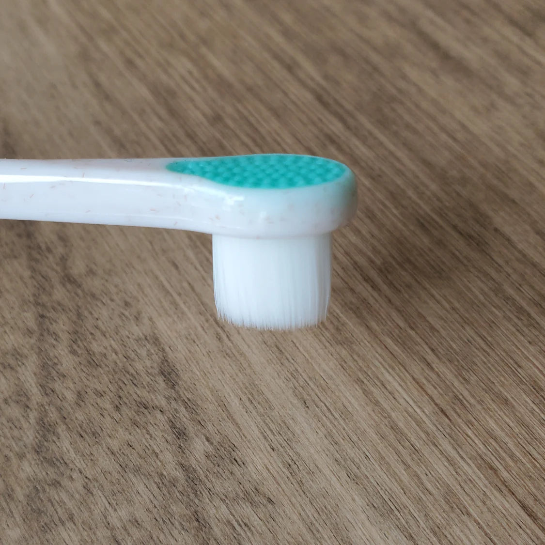Close-up of a Puppy Polisher toothbrush with ultra-fine white bristles and a teal tongue cleaner.