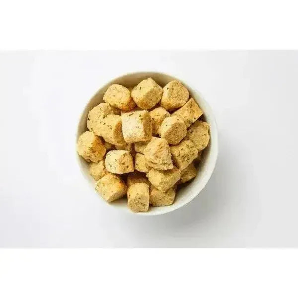 Overhead view of a white bowl filled with cube-shaped freeze-dried raw chicken dog and cat treats with spinach flecks.