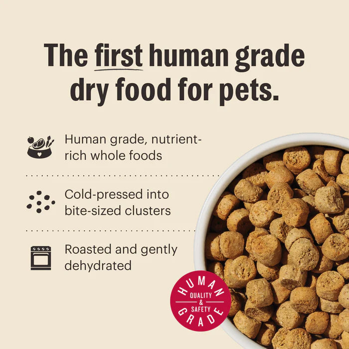 A bowl of dry dog food clusters with text describing human grade, cold-pressed, and roasted food.