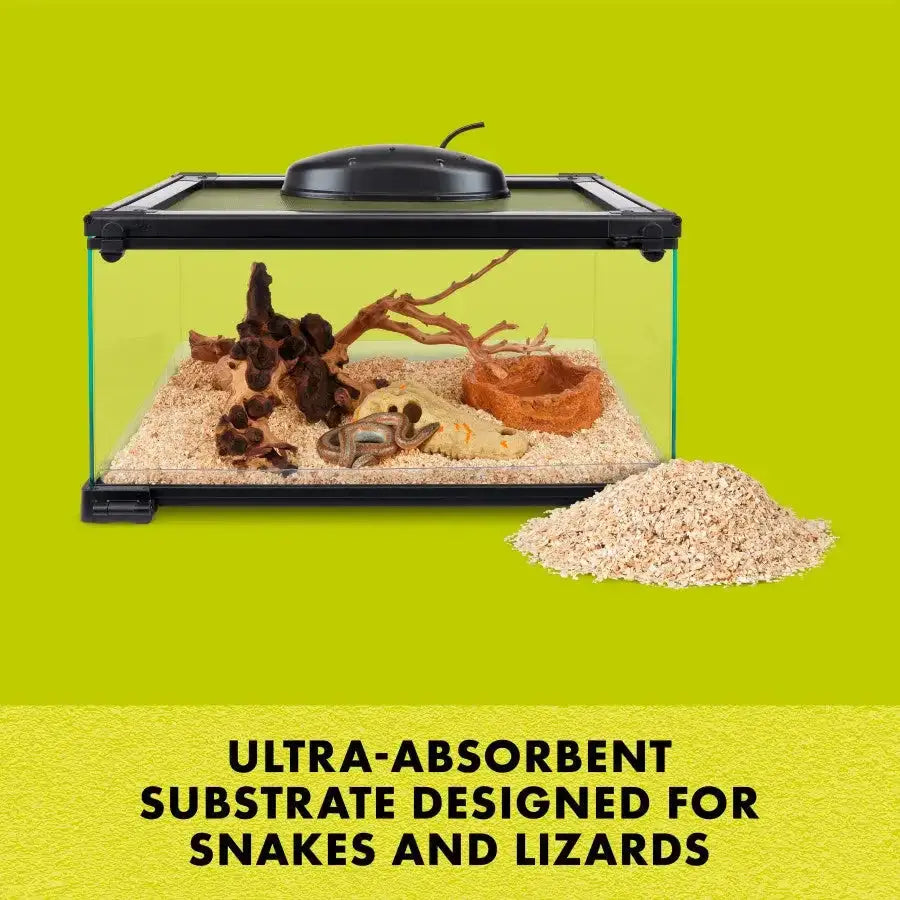 A glass terrarium with a black lid sits against a lime green background, featuring branches and rocks. Outside, theres Zilla® Snake Bedding Lizard Litter Natural. Text reads: Ultra-absorbent substrate designed for snakes and lizards.